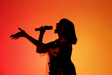 Image showing Silhouette of young caucasian female singer isolated on orange gradient studio background in neon light