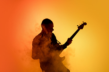 Image showing Silhouette of young caucasian male guitarist isolated on orange gradient studio background in neon light