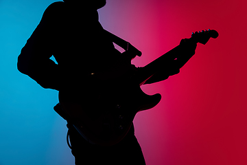 Image showing Silhouette of young caucasian male guitarist isolated on blue-pink gradient studio background in neon light