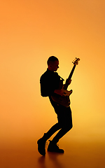 Image showing Silhouette of young caucasian male guitarist isolated on orange gradient studio background in neon light