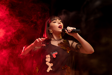 Image showing Caucasian female singer portrait isolated on dark studio background in neon light