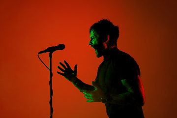 Image showing Silhouette of young caucasian male singer isolated on orange gradient studio background in neon light