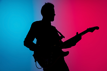 Image showing Silhouette of young caucasian male guitarist isolated on blue-pink gradient studio background in neon light