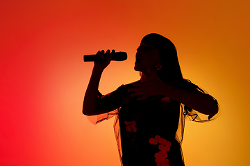 Image showing Silhouette of young caucasian female singer isolated on orange gradient studio background in neon light