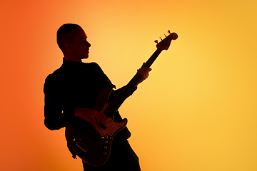 Image showing Silhouette of young caucasian male guitarist isolated on orange gradient studio background in neon light