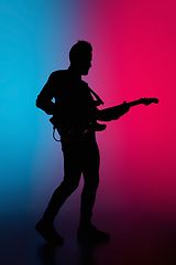 Image showing Silhouette of young caucasian male guitarist isolated on blue-pink gradient studio background in neon light