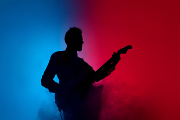 Image showing Silhouette of young caucasian male guitarist isolated on blue-pink gradient studio background in neon light