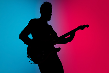 Image showing Silhouette of young caucasian male guitarist isolated on blue-pink gradient studio background in neon light