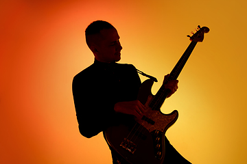 Image showing Silhouette of young caucasian male guitarist isolated on orange gradient studio background in neon light