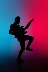 Image showing Silhouette of young caucasian male guitarist isolated on blue-pink gradient studio background in neon light