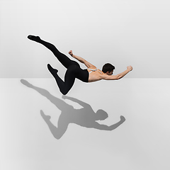 Image showing Beautiful young male athlete practicing on white studio background with shadows in jump, air flying