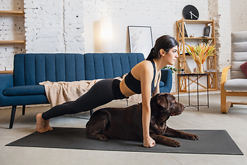 Image showing Young woman working out at home during lockdown, yoga exercises with the dog