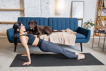 Image showing Young woman working out at home during lockdown, yoga exercises with the dog