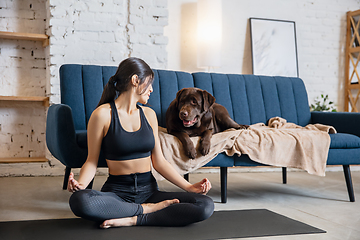 Image showing Young woman working out at home during lockdown, yoga exercises with the dog