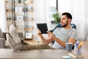 Image showing man with tablet pc resting feet on table at home