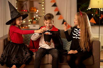 Image showing kids in halloween costumes share candies at home