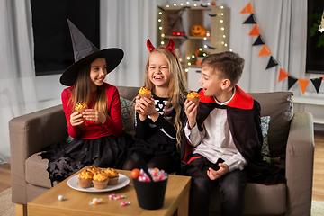 Image showing kids in halloween costumes eating cupcakes at home