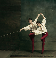 Image showing Two young female ballet dancers like duelists with swords. Ballet and contemporary choreography concept. Creative art photo.