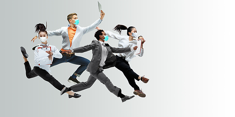 Image showing Happy office workers in face masks jumping and dancing in casual clothes or suit isolated on studio background. Creative collage.