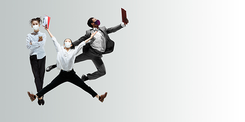 Image showing Happy office workers in face masks jumping and dancing in casual clothes or suit isolated on studio background. Creative collage.