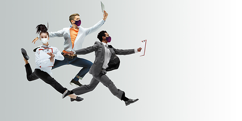 Image showing Happy office workers in face masks jumping and dancing in casual clothes or suit isolated on studio background. Creative collage.