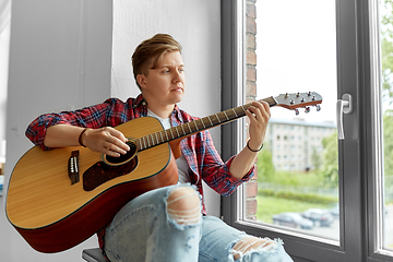 Image showing young man playing guitar sitting on windowsill