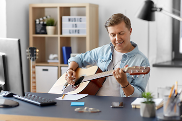 Image showing young man playing guitar sitting at table at home