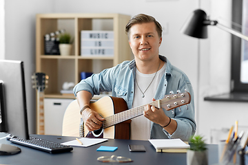 Image showing young man playing guitar sitting at table at home