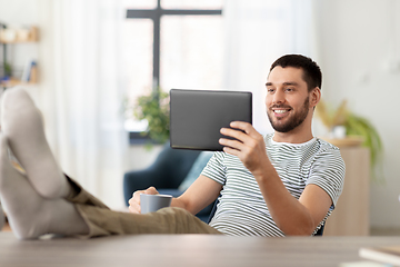 Image showing man with tablet pc resting feet on table at home