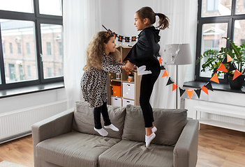 Image showing girls in halloween costumes jumping on sofa