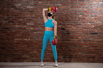 Image showing Professional female athlete training on brick wall background wearing face mask. Sport during quarantine