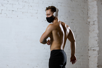 Image showing Professional male athlete training on brick wall background wearing face mask. Sport during quarantine