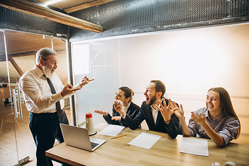 Image showing Angry boss with megaphone screaming at employees in office, scared and annoyed colleagues listening at the table