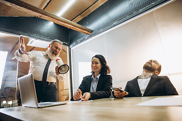 Image showing Angry boss with megaphone screaming at employees in office, scared and annoyed colleagues listening at the table