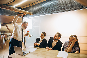 Image showing Angry boss with megaphone screaming at employees in office, scared and annoyed colleagues listening at the table