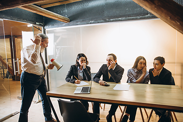 Image showing Angry boss with megaphone screaming at employees in office, scared and annoyed colleagues listening at the table