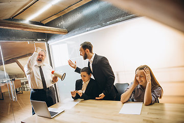 Image showing Angry boss with megaphone screaming at employees in office, scared and annoyed colleagues listening at the table