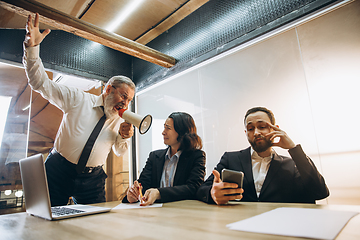 Image showing Angry boss with megaphone screaming at employees in office, scared and annoyed colleagues listening at the table