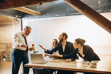 Image showing Angry boss with megaphone screaming at employees in office, scared and annoyed colleagues listening at the table