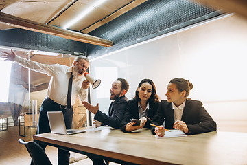 Image showing Angry boss with megaphone screaming at employees in office, scared and annoyed colleagues listening at the table