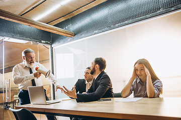 Image showing Angry boss with megaphone screaming at employees in office, scared and annoyed colleagues listening at the table