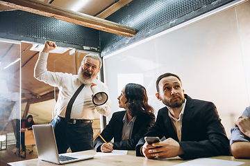 Image showing Angry boss with megaphone screaming at employees in office, scared and annoyed colleagues listening at the table