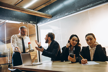 Image showing Angry boss with megaphone screaming at employees in office, scared and annoyed colleagues listening at the table