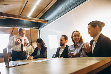 Image showing Angry boss with megaphone screaming at employees in office, scared and annoyed colleagues listening at the table