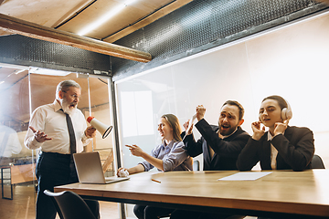 Image showing Angry boss with megaphone screaming at employees in office, scared and annoyed colleagues listening at the table