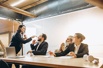 Image showing Angry boss with megaphone screaming at employees in office, scared and annoyed colleagues listening at the table