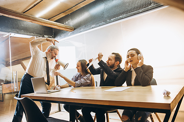 Image showing Angry boss with megaphone screaming at employees in office, scared and annoyed colleagues listening at the table