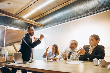 Image showing Angry boss with megaphone screaming at employees in office, scared and annoyed colleagues listening at the table