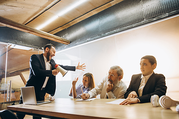 Image showing Angry boss with megaphone screaming at employees in office, scared and annoyed colleagues listening at the table