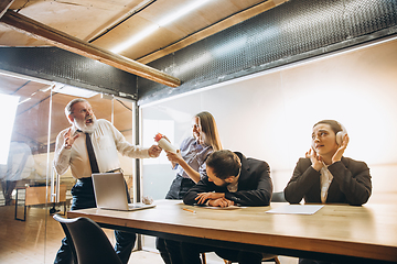 Image showing Angry boss with megaphone screaming at employees in office, scared and annoyed colleagues listening at the table